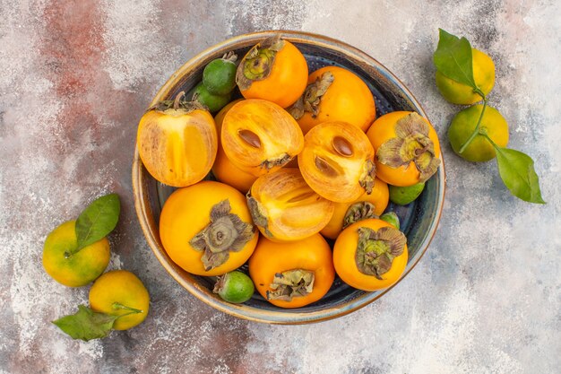 Vue de dessus des kakis frais feykhoas dans un bol et des mandarines sur fond nu