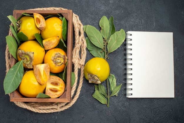 Vue de dessus des kakis sucrés frais à l'intérieur de la boîte sur le goût de fruits mûrs table sombre