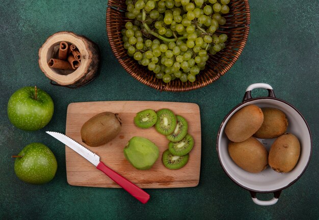 Vue de dessus kiwi dans une casserole avec des tranches et un couteau sur un support avec des pommes et des raisins à la cannelle sur fond vert
