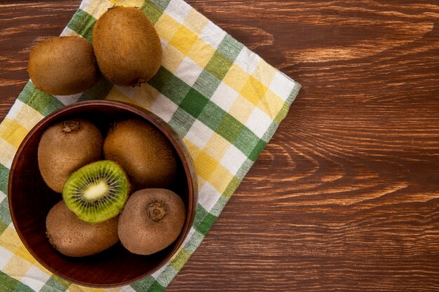 Vue de dessus des kiwis frais dans un bol en bois sur une serviette de table à carreaux sur bois avec copie espace