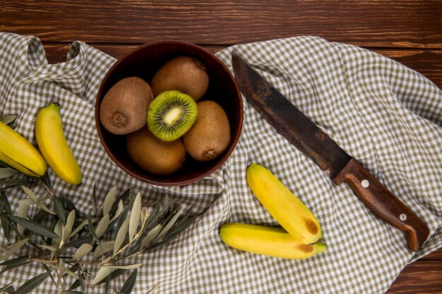 Vue de dessus des kiwis mûrs frais dans un bol en bois et des bananes fraîches avec un vieux couteau de cuisine rustique