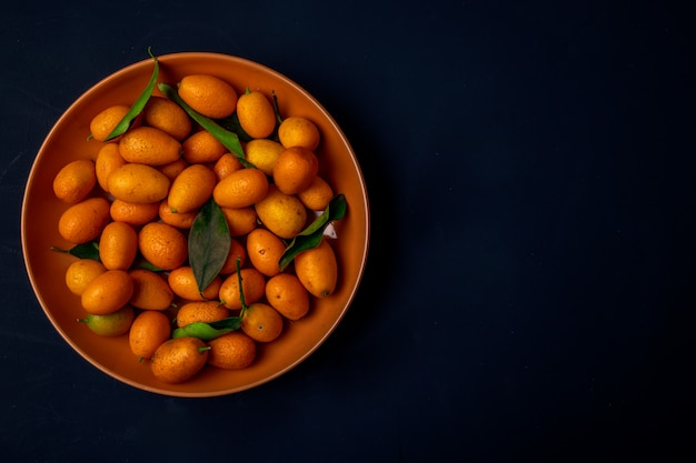 Vue de dessus des kumquats mûrs frais sur une plaque sur une surface noire avec copie espace