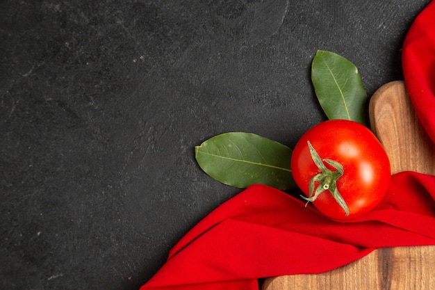 Vue de dessus un laurier de tomate laisse une serviette rouge et une planche à découper sur un sol sombre