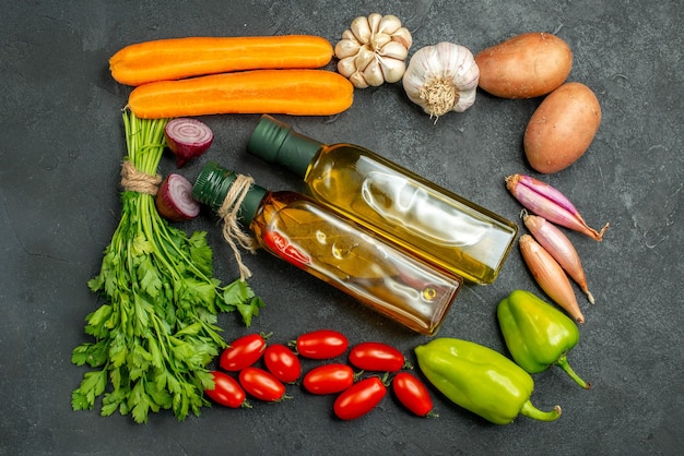 Vue de dessus des légumes en carré et avec des bouteilles d'huile au centre sur fond gris foncé