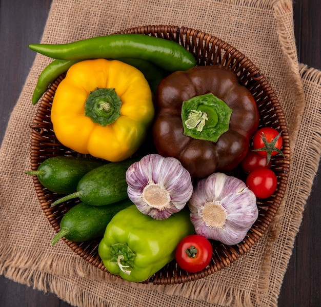 Vue de dessus des légumes comme l'ail concombre tomate poivron dans le panier sur un sac et une surface en bois