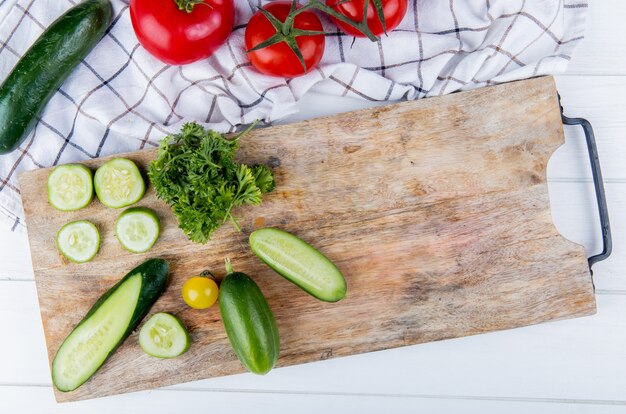 Vue de dessus des légumes comme concombre tomate coriandre sur planche à découper avec concombre et tomates sur tissu et bois