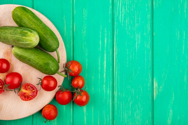 Vue de dessus des légumes comme le concombre et la tomate sur une planche à découper sur une surface verte