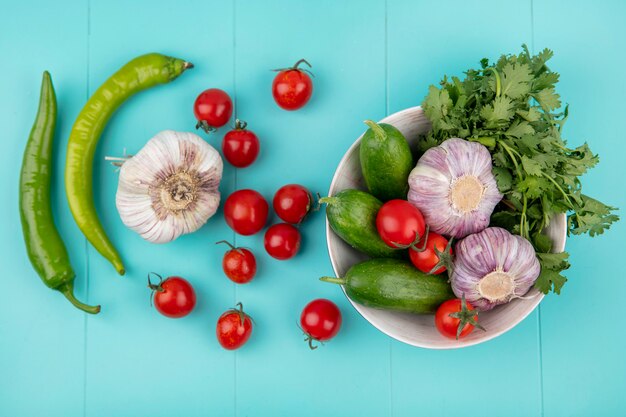 Vue de dessus des légumes comme la coriandre concombre tomate et l'ail dans un bol avec des poivrons sur une surface bleue