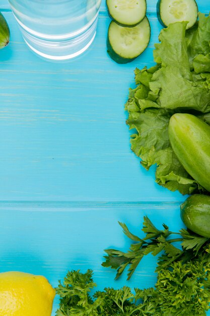 Vue de dessus des légumes comme la coriandre de laitue de concombre avec de l'eau détox et du citron sur la surface bleue