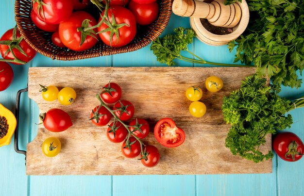 Vue de dessus des légumes comme la coriandre tomate sur une planche à découper avec broyeur d'ail poivre noir sur bleu