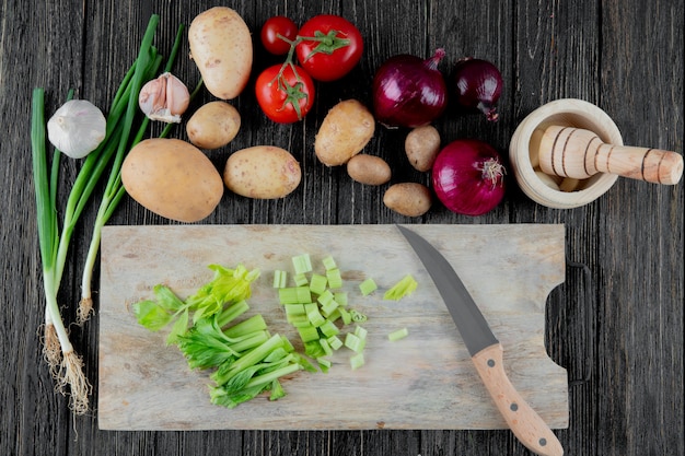 Vue de dessus des légumes comme oignon d'ail de pomme de terre échalote avec du céleri coupé sur une planche à découper sur fond de bois