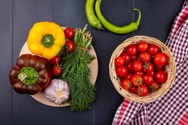 Vue de dessus des légumes comme panier de tomates sur tissu à carreaux avec poivron tomate ail bouquet d'aneth sur une planche à découper sur une surface noire