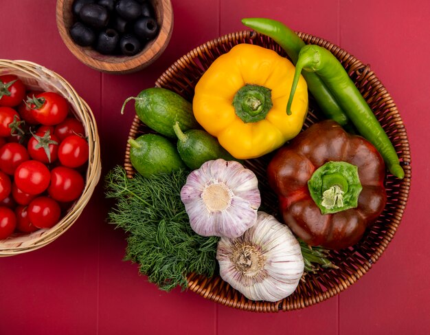 Vue de dessus des légumes comme poivron concombre tomate ail aneth avec olive dans des paniers sur la surface rouge