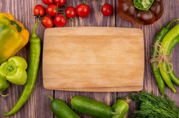 Vue de dessus des légumes comme tas de poivron de concombre tomate aneth autour d'une planche à découper sur une surface en bois