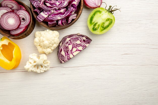 Vue de dessus légumes coupés chou rouge tomate verte citrouille oignon rouge poivron chou-fleur citron dans des bols en bois sur une surface en bois blanc avec copie place