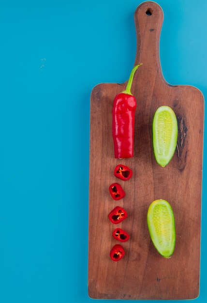 Photo gratuite vue de dessus des légumes coupés et tranchés comme du poivre et du concombre sur une planche à découper et une surface bleue avec copie espace