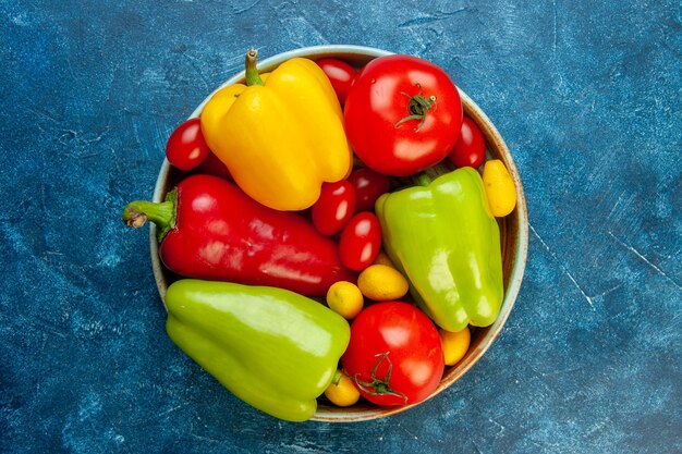 Vue de dessus légumes différentes couleurs poivrons tomates tomates cerises dans un bol sur table bleue avec espace copie