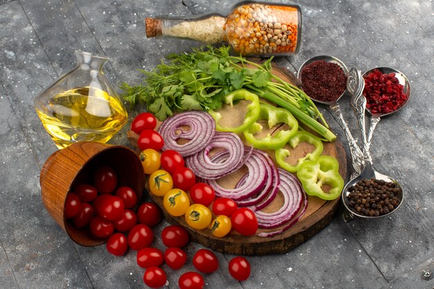 Vue de dessus des légumes entiers tranchés tels que les oignons, les poivrons verts, les tomates sur le bureau en bois brun et le sol gris