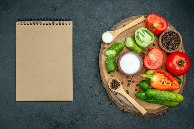 Vue de dessus légumes frais concombre haché poivre noir et sel dans une cuillère en bois sur planche de bois sur fond sombre