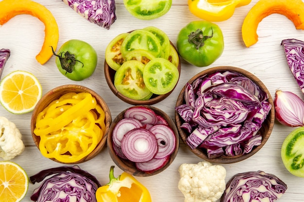 Vue de dessus légumes frais coupés chou rouge tomate verte citrouille oignon rouge poivron jaune chou-fleur citron dans de petits bols sur une surface blanche