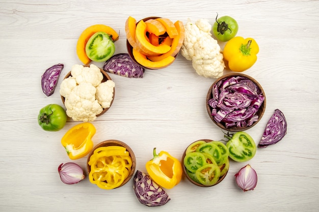 Vue De Dessus Légumes Frais Coupés Tomates Vertes Chou Rouge Oignon Potiron Chou-fleur Poivron Jaune Dans Des Bols Sur Une Surface En Bois Blanc Avec Espace Libre