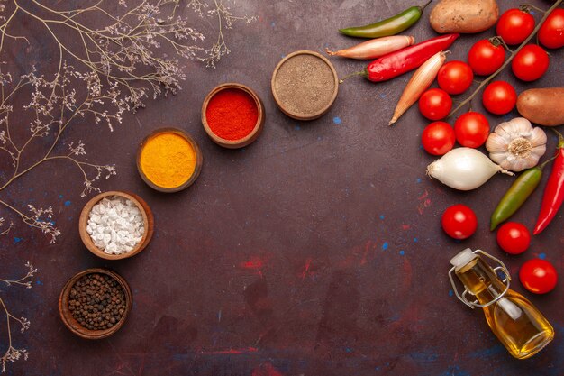 Vue de dessus des légumes frais avec différents assaisonnements sur un bureau sombre