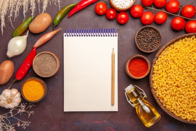 Vue de dessus des légumes frais avec différents assaisonnements et pâtes sur un bureau sombre