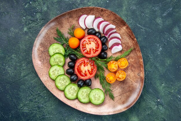 Vue de dessus des légumes frais hachés olives kumquats dans une assiette brune sur fond de couleurs mélangées noir vert