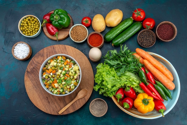 Vue de dessus des légumes frais avec des légumes verts et des assaisonnements sur la nourriture végétale de salade de collation de bureau bleu