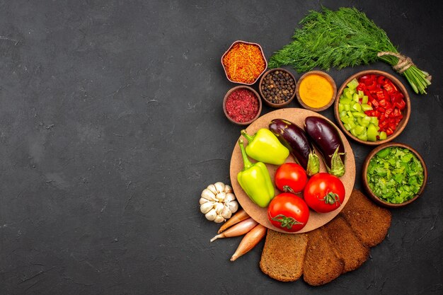 Vue de dessus des légumes frais mûrs avec des verts et des miches de pain noir sur la surface sombre salade alimentaire repas santé légume