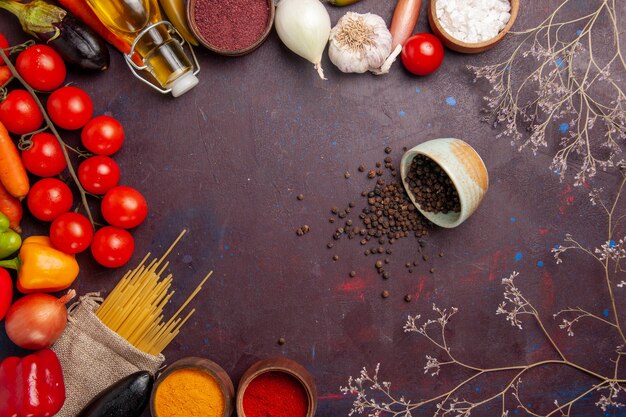 Vue de dessus des légumes frais avec des pâtes italiennes crues et des assaisonnements sur l'espace sombre