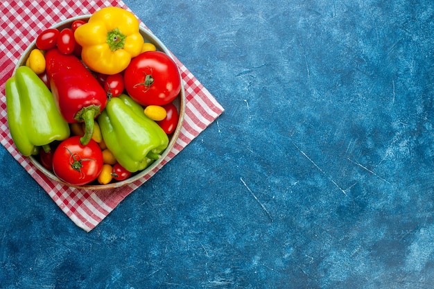 Vue de dessus légumes frais tomates cerises différentes couleurs poivrons tomates cumcuat sur plateau sur une serviette de cuisine à carreaux blanc rouge sur table bleue avec espace de copie