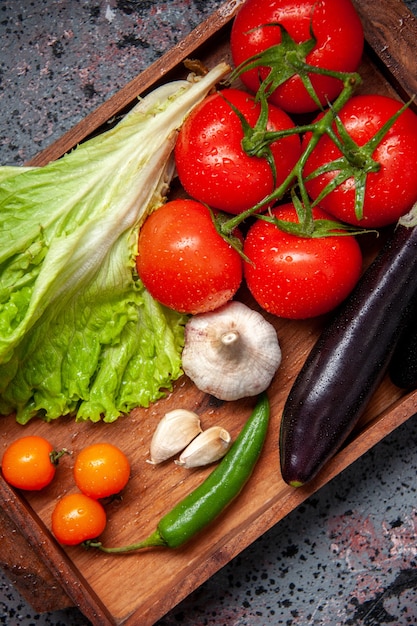 Vue de dessus légumes frais tomates rouges ail salade verte et aubergines à l'intérieur de la planche de bois sur la surface bleue salade repas repas couleur mûre