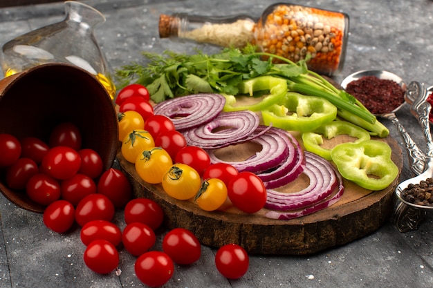 Vue de dessus des légumes frais en tranches comme les oignons, le poivron vert et les tomates sur le gris