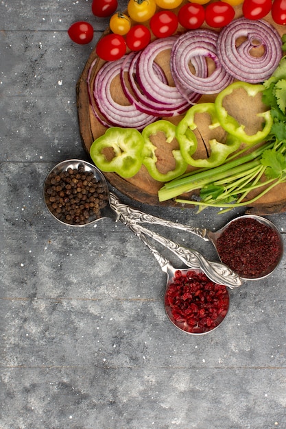 Photo gratuite vue de dessus des légumes frais tranchés tels que les oignons tomates poivrons verts sur le sol gris