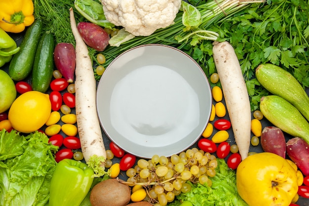 Vue de dessus légumes et fruits tomates cerises laitue cumcuat coing raisin citron chou-fleur radis blanc persil courgettes assiette au centre