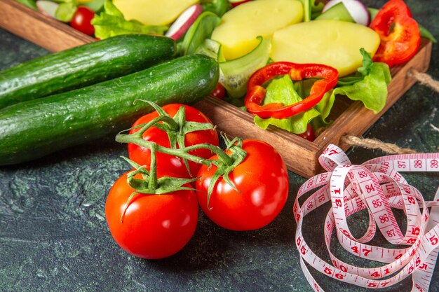 Vue de dessus de légumes hachés tomates fraîches avec mètre de tige et concombres sur un plateau en bois sur la surface des couleurs de mélange