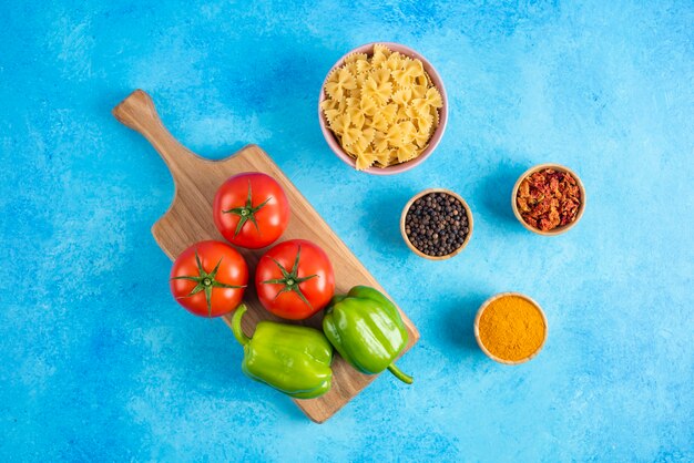 Vue de dessus. Légumes sur planche de bois et épices avec pâtes crues sur surface bleue.