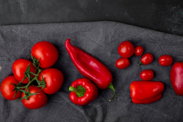 Vue de dessus des légumes sous forme de tomates et de poivrons entiers sur une surface en tissu et une surface noire