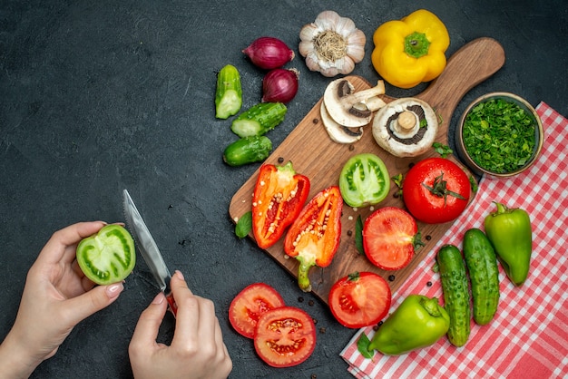 Vue de dessus légumes tomates poivrons sur planche à découper verts dans un bol concombres sur nappe rouge