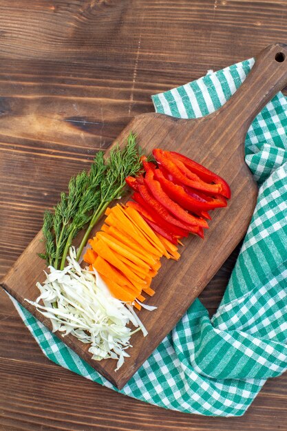 Vue de dessus légumes tranchés chou carottes verts et poivron sur planche à découper surface brune