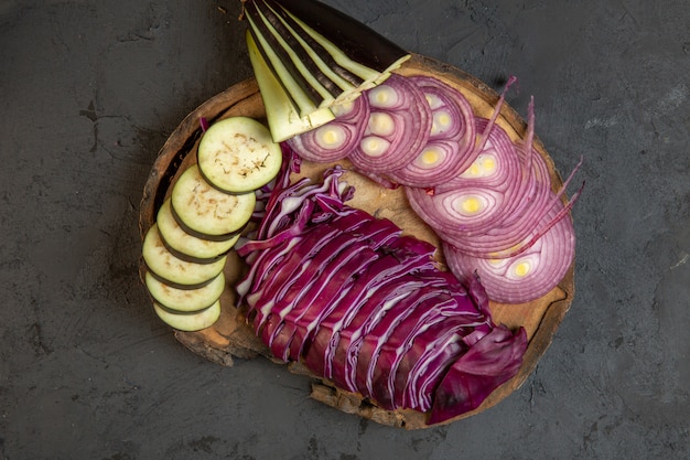 Vue de dessus des légumes en tranches de chou oignon rouge et aubergine sur une planche de bois sur fond noir