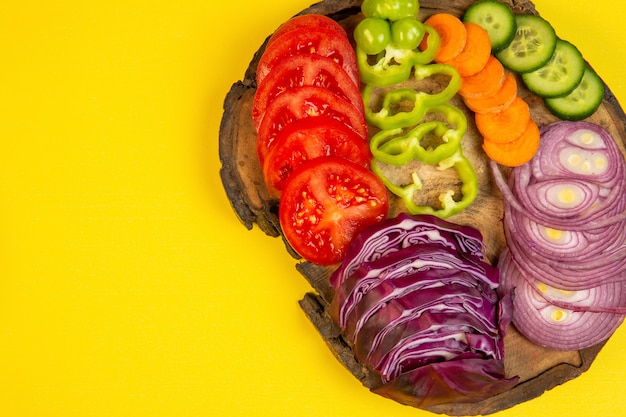 Vue de dessus de légumes en tranches de chou rouge tomates oignon poivrons carotte et concombres sur une planche de bois sur jaune j