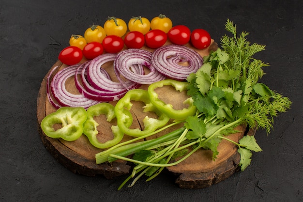 Vue de dessus des légumes tranchés et de couleur entière avec des verts sur le bureau en bois brun sur le sol sombre