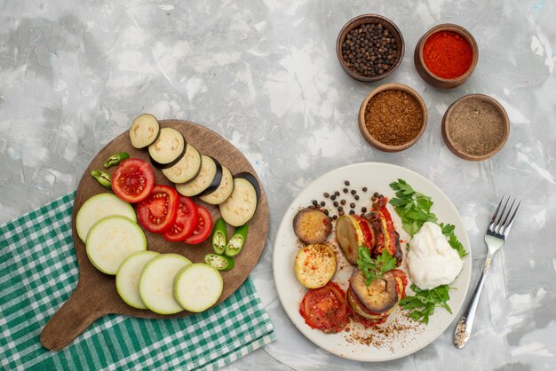 Vue de dessus des légumes tranchés tels que les aubergines et les tomates avec des légumes cuits sur le plat de repas de couleur végétale de bureau lumineux