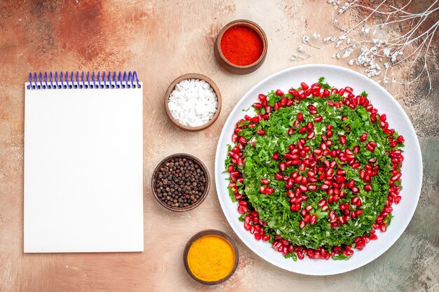 Vue de dessus des légumes verts frais avec des grenades pelées sur un repas au sol clair couleur des fruits vert