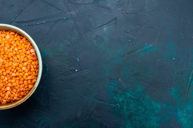 Vue de dessus de la lentille orange crue à l'intérieur du pot rond sur la surface bleu foncé