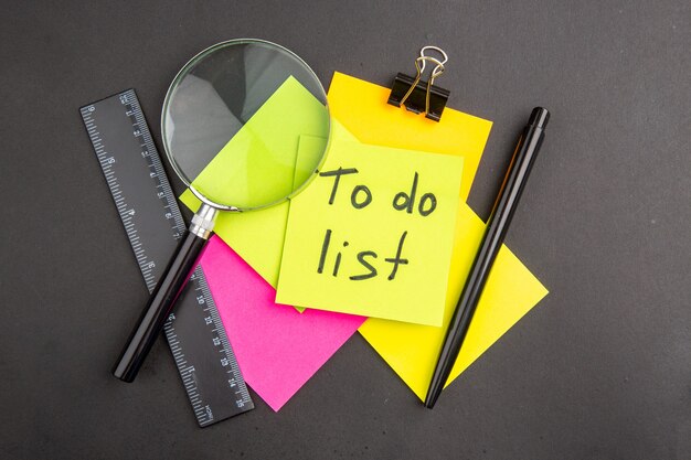Vue de dessus de la liste de tâches écrite sur une note collante jaune Notes collantes colorées Règle de stylo lupa sur noir