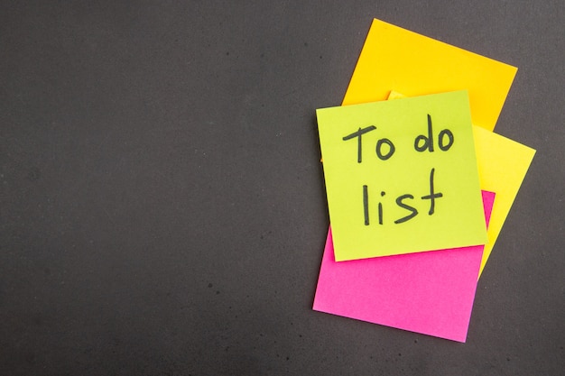 Vue de dessus de la liste de tâches écrite sur une note collante verte Notes collantes colorées sur noir avec lieu de copie