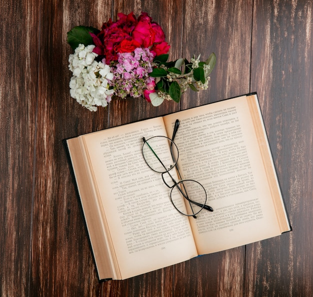 Photo gratuite vue de dessus livre ouvert avec des lunettes optiques et des fleurs sur un fond en bois